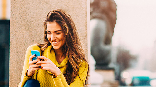 Código Descuento Girl looking at her phone and laughing while checking a discount code to fly with Iberia